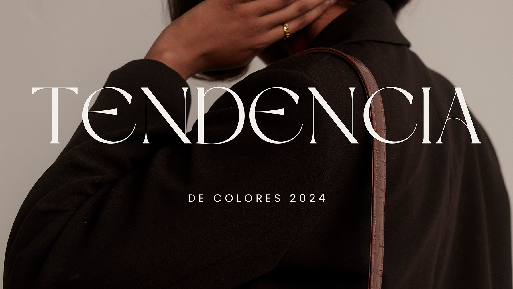 La imagen es una fotografía artística que presenta la portada de un artículo de moda sobre tendencias de color para el año 2024. En la foto, se puede ver una persona de espaldas, vestida con una prenda de color oscuro. El fondo es neutro, lo que resalta el texto en la imagen. El texto principal dice "TENDENCIA" en una tipografía elegante y moderna, mientras que el subtítulo dice "DE COLORES 2024" en letras más pequeñas. La composición es sofisticada y minimalista, enfocándose en la moda y las tendencias actuales.